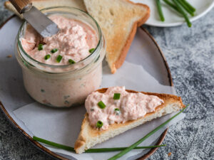 Salmon and soft creme cheese spread in jar. Salmon rillettes, mousse, pate and toasts on gray background